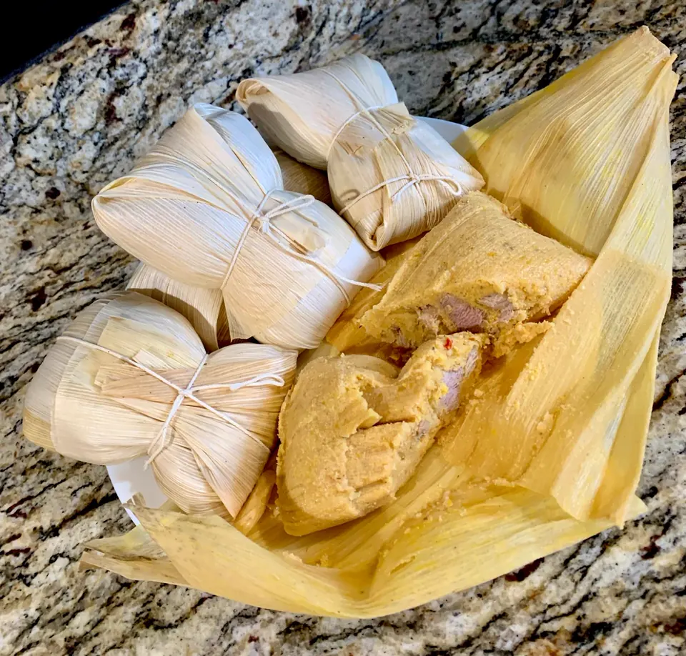 Cuban tamales in corn husks, one unwrapped to show the filling